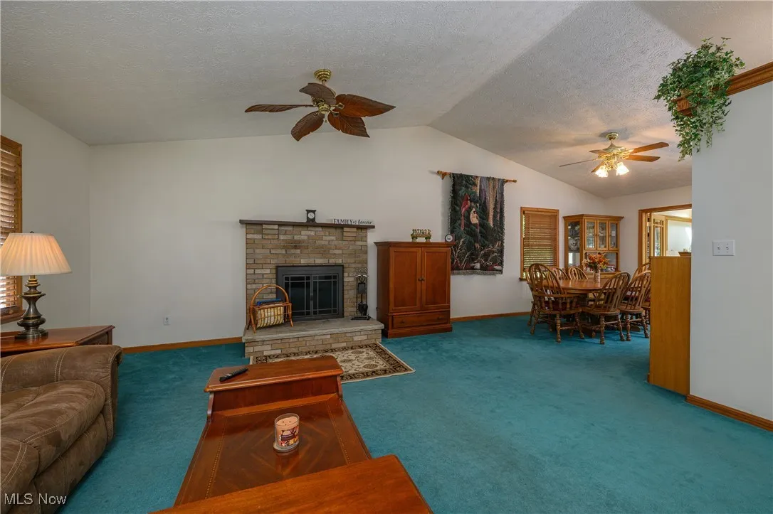 Carpeted living room featuring a brick fireplace, a ceiling fan, a textured ceiling, and lofted ceiling