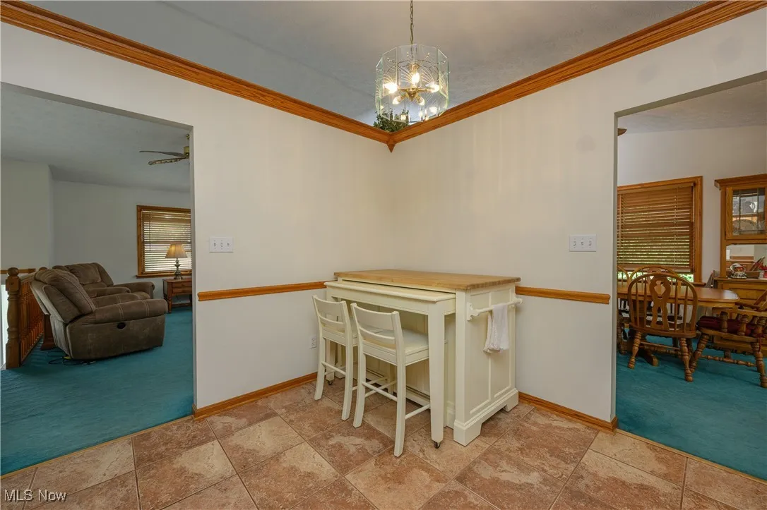 Dining area with light colored carpet, ornamental molding, and a chandelier