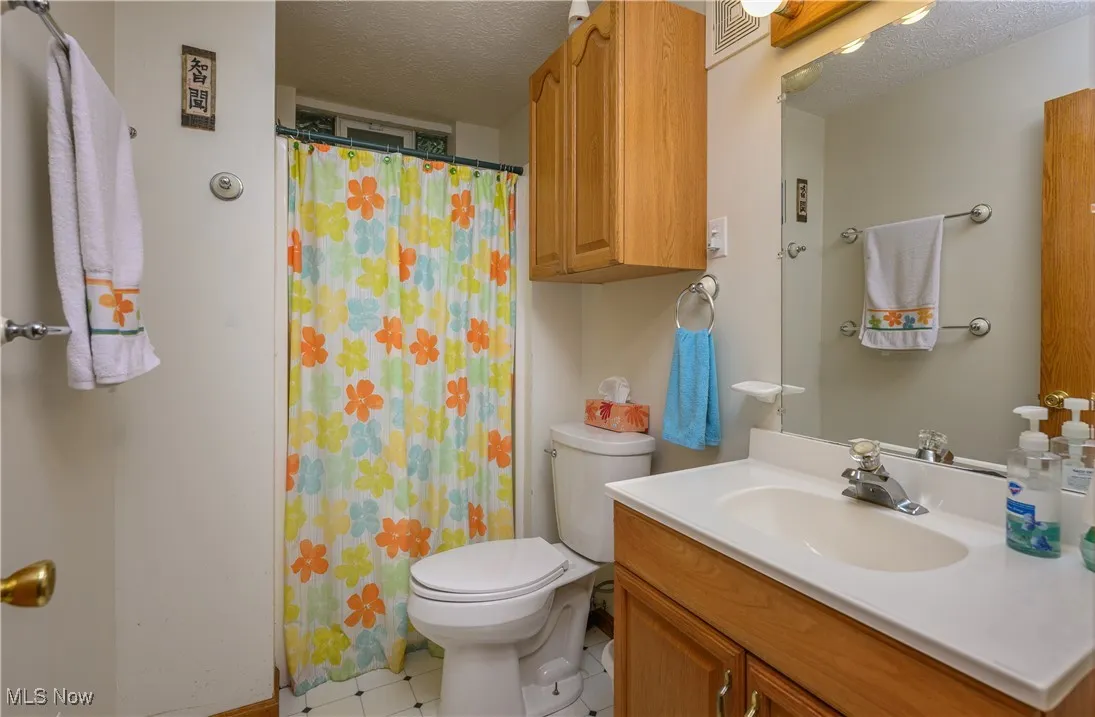 Bathroom with a textured ceiling, vanity, light tile patterned floors, and curtained shower