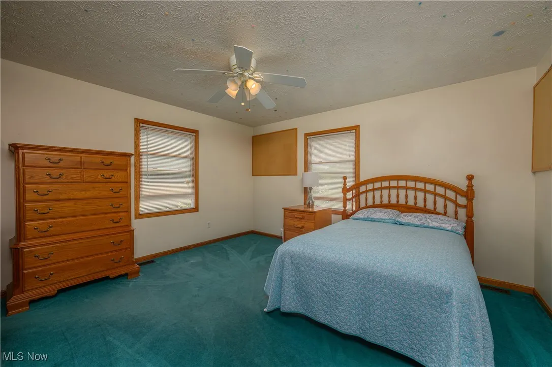 Bedroom with a textured ceiling, carpet, multiple windows, and a ceiling fan