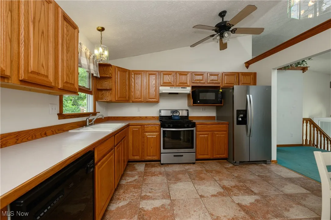 Kitchen featuring a chandelier, black appliances, vaulted ceiling, decorative light fixtures, and light countertops
