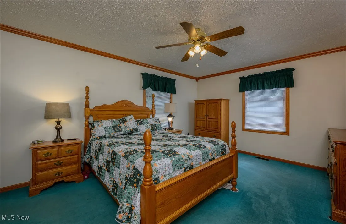 Carpeted bedroom with crown molding, a textured ceiling, and ceiling fan