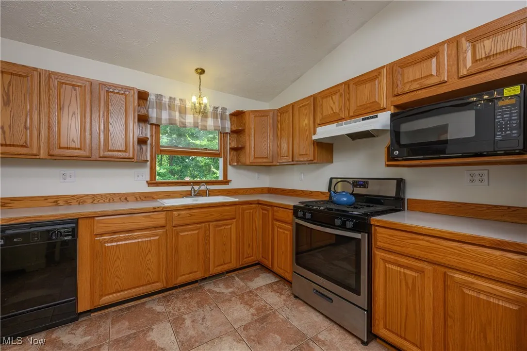 Kitchen featuring lofted ceiling, black appliances, light countertops, brown cabinets, and a textured ceiling