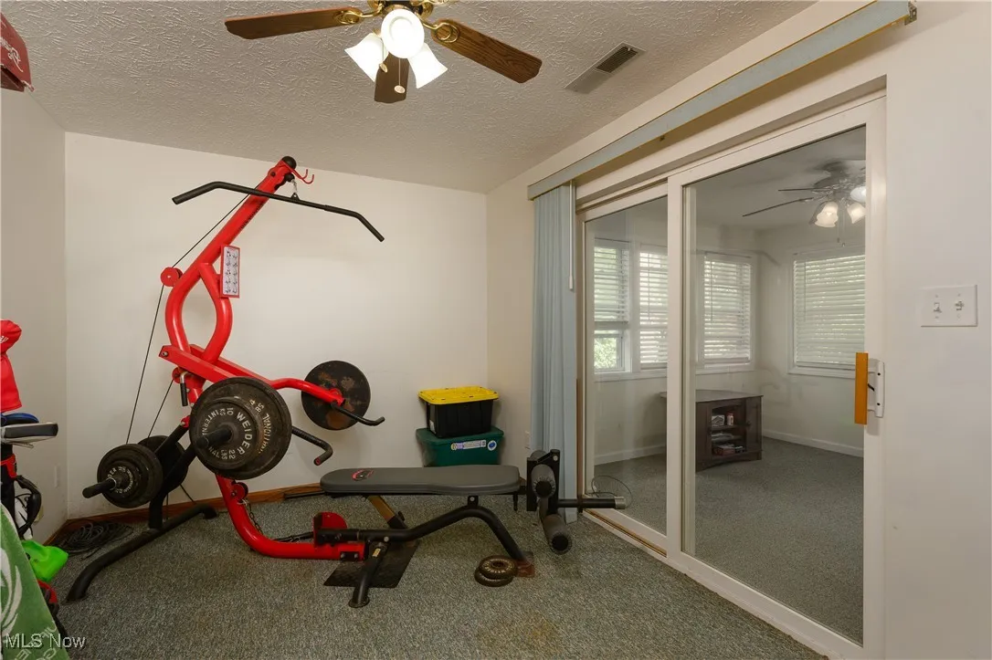Exercise area featuring a ceiling fan, a textured ceiling, and carpet floors