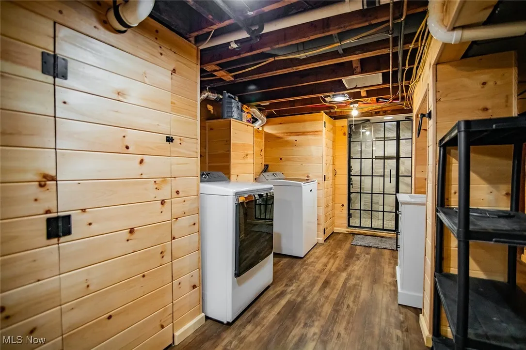 Laundry area featuring wooden walls, dark wood-style floors, and washing machine and dryer