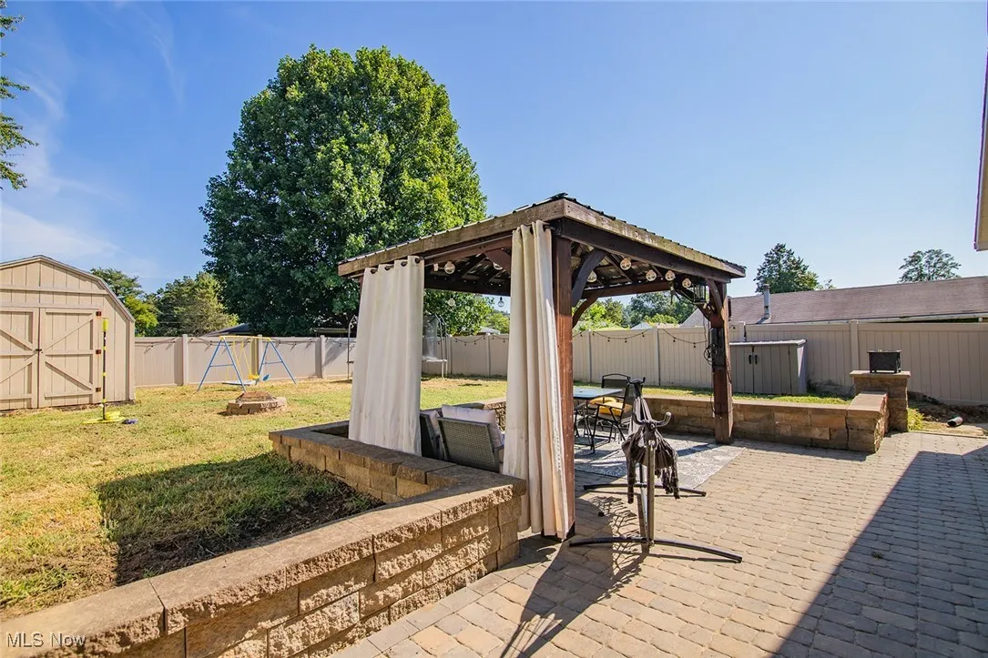 Fenced backyard with a storage shed, a gazebo, a patio area, and a fire pit