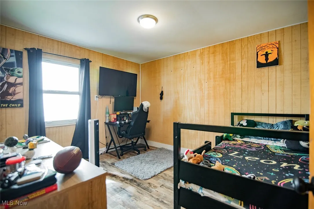 Bedroom with a desk, wood finished floors, and wooden walls