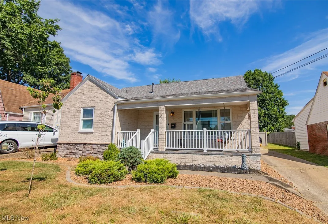 View of front of house with stone siding, covered porch, and a shingled roof
