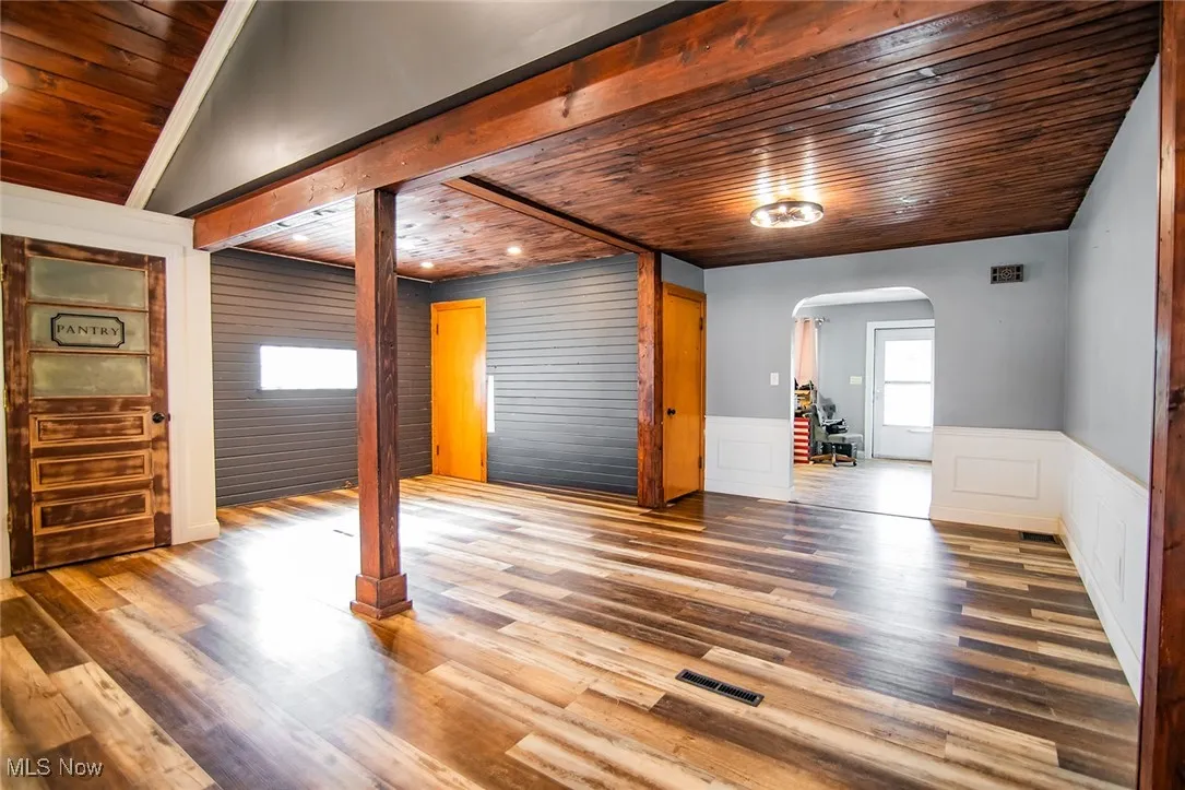 Unfurnished living room with wooden ceiling, arched walkways, wood finished floors, a wainscoted wall, and a decorative wall