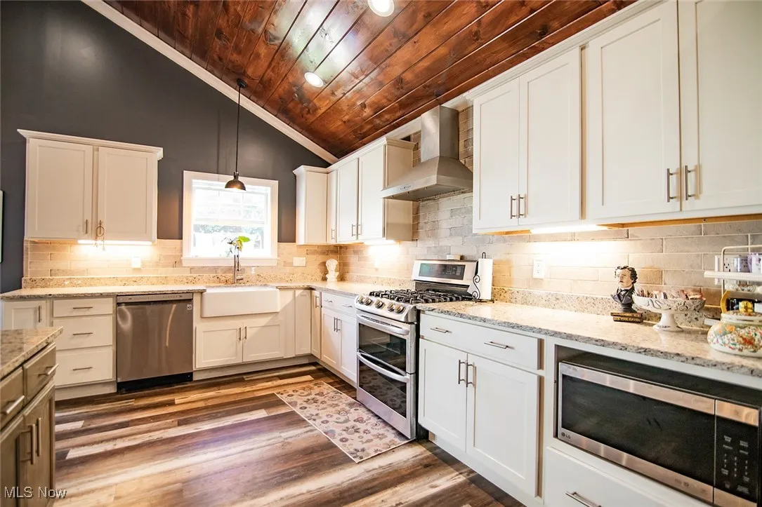 Kitchen featuring stainless steel appliances, wooden ceiling, wall chimney exhaust hood, vaulted ceiling, and white cabinetry