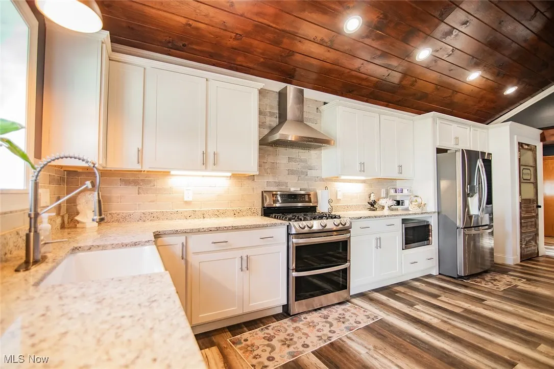 Kitchen featuring appliances with stainless steel finishes, wall chimney exhaust hood, wooden ceiling, white cabinetry, and recessed lighting