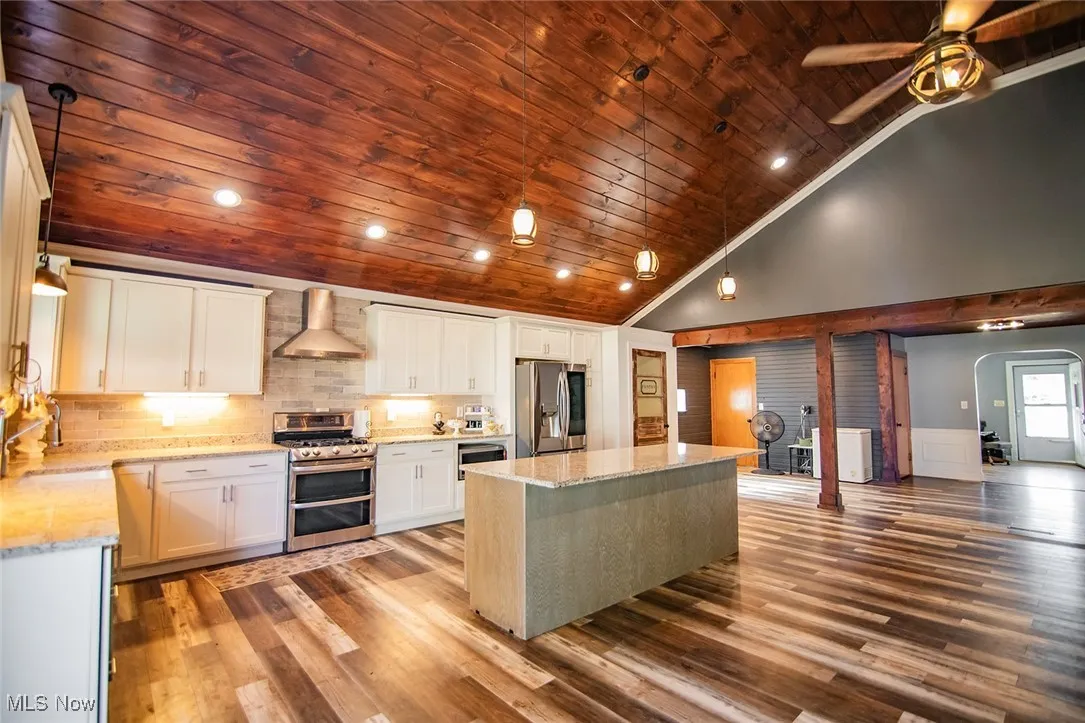 Kitchen with wood ceiling, recessed lighting, appliances with stainless steel finishes, light stone counters, and wall chimney exhaust hood