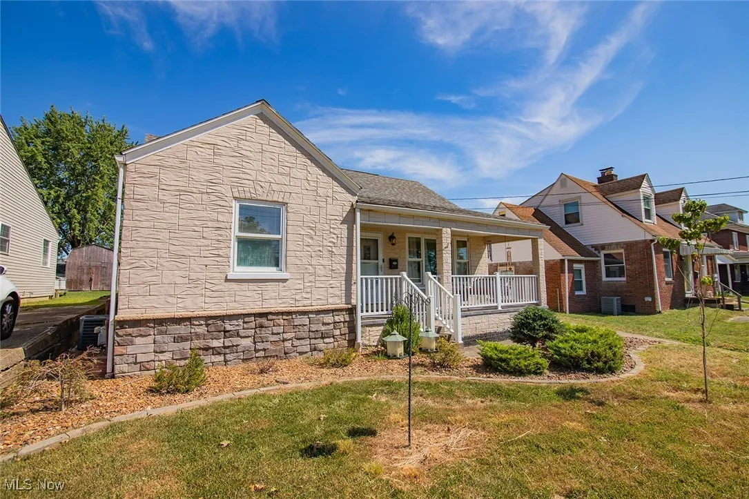 View of front of home with covered porch, stone siding, and a front lawn