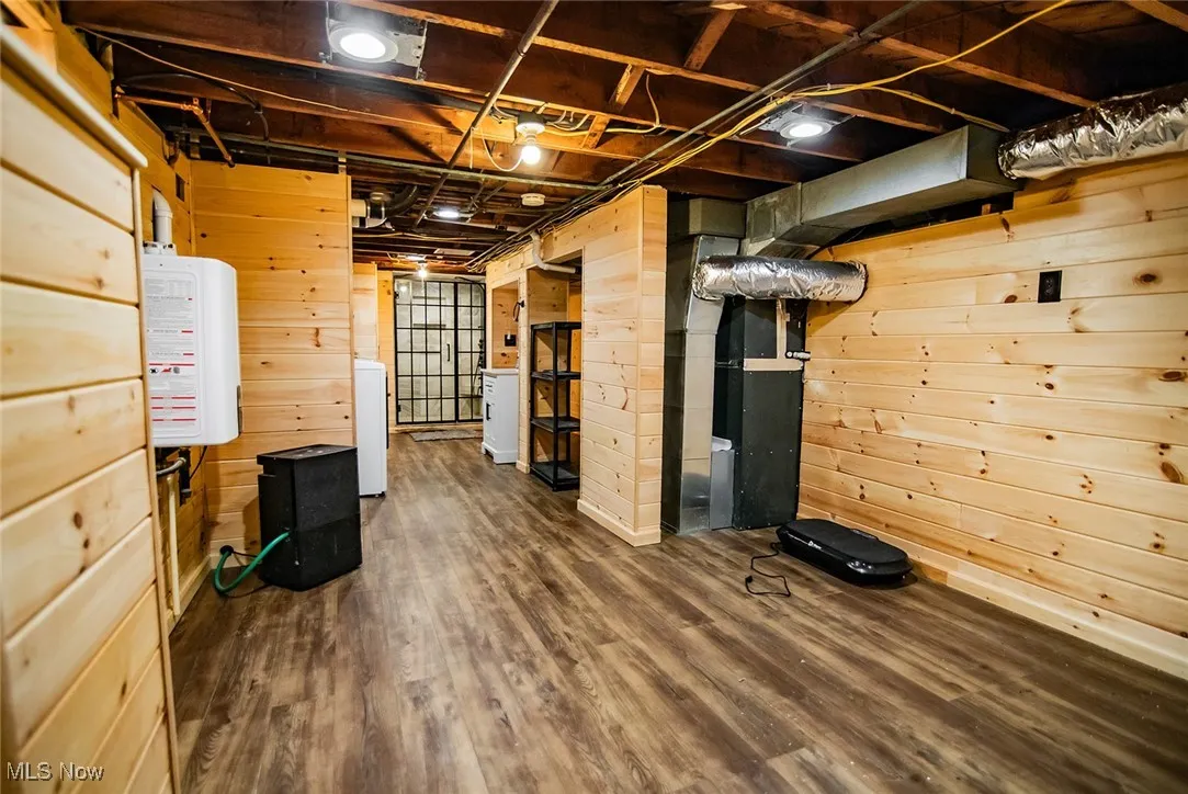 Unfinished below grade area with wood walls, dark wood finished floors, heating unit, and washer / dryer