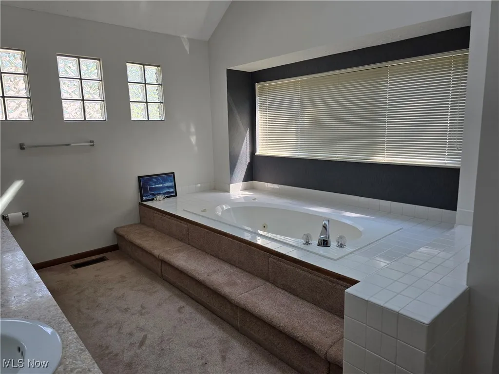Bathroom with a jetted tub, double vanity, and vaulted ceiling
