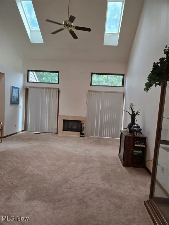 Carpeted living area with a skylight, plenty of natural light, high vaulted ceiling, and a fireplace