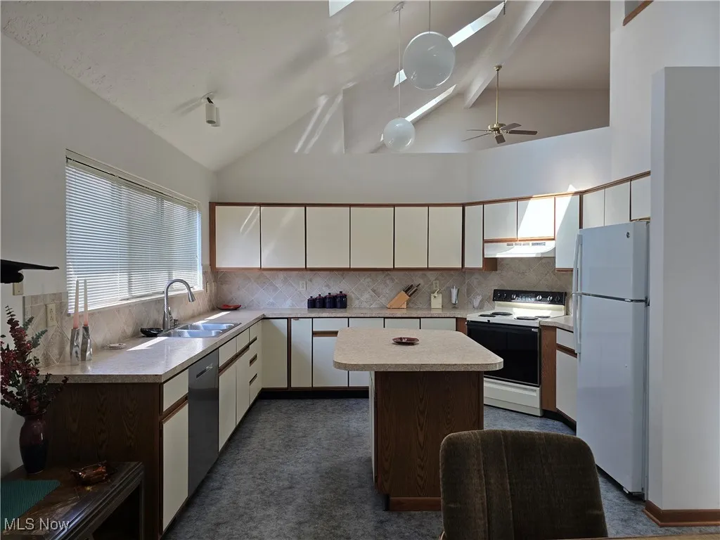 Kitchen featuring decorative backsplash, light countertops, a skylight, white cabinets, and appliances
