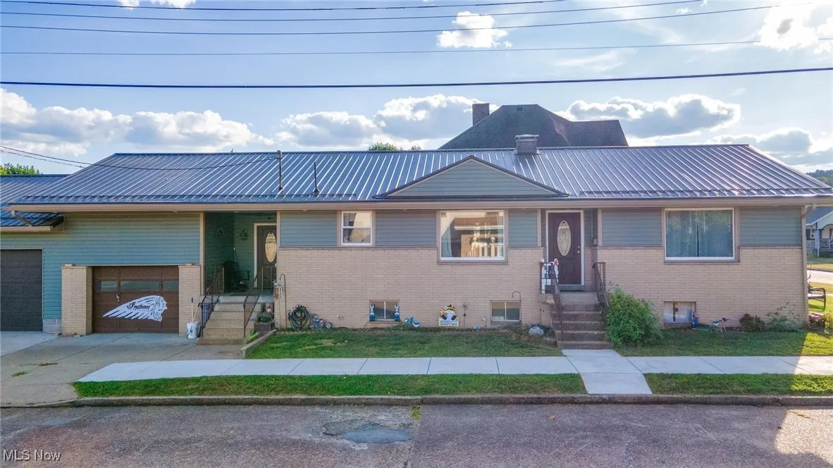 View of front facade with a metal roof, a chimney, brick siding, a standing seam roof, and an attached garage