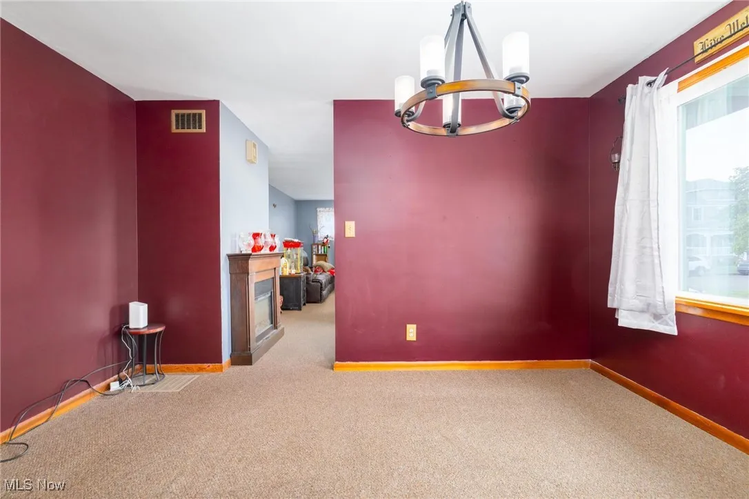 Carpeted spare room featuring a fireplace and a chandelier