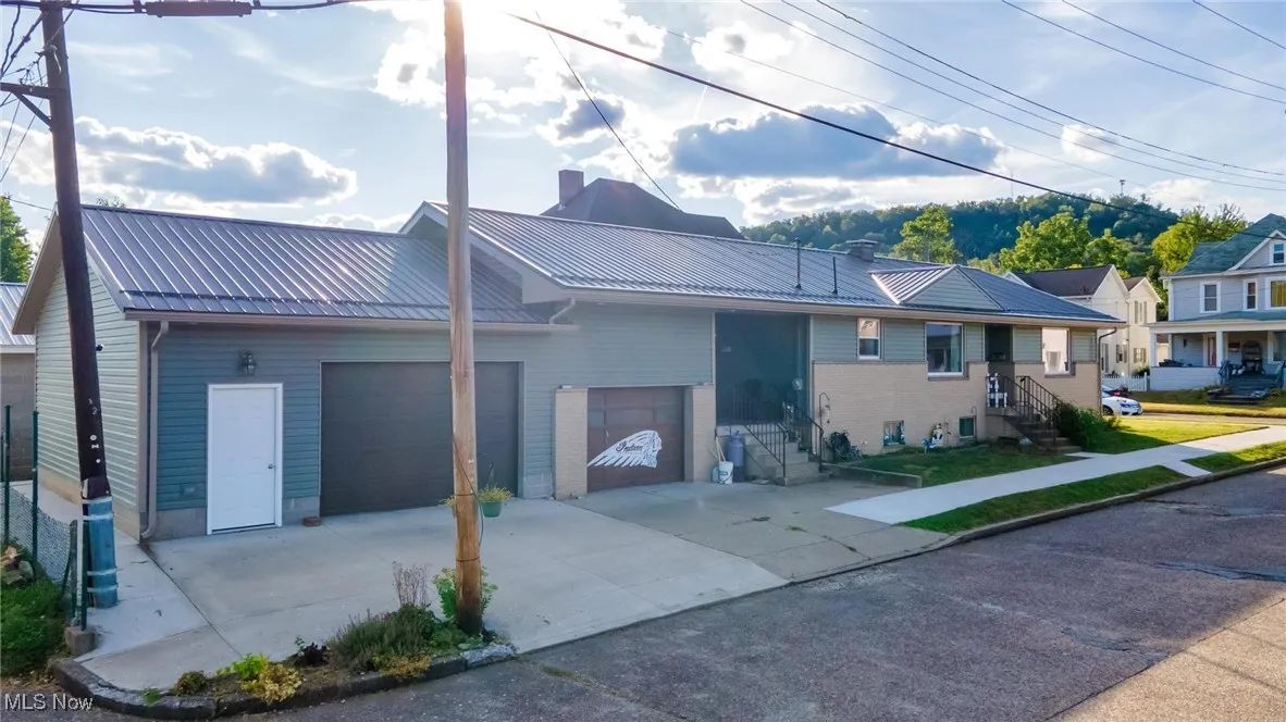 View of front facade featuring concrete driveway, a metal roof, a garage, and a chimney