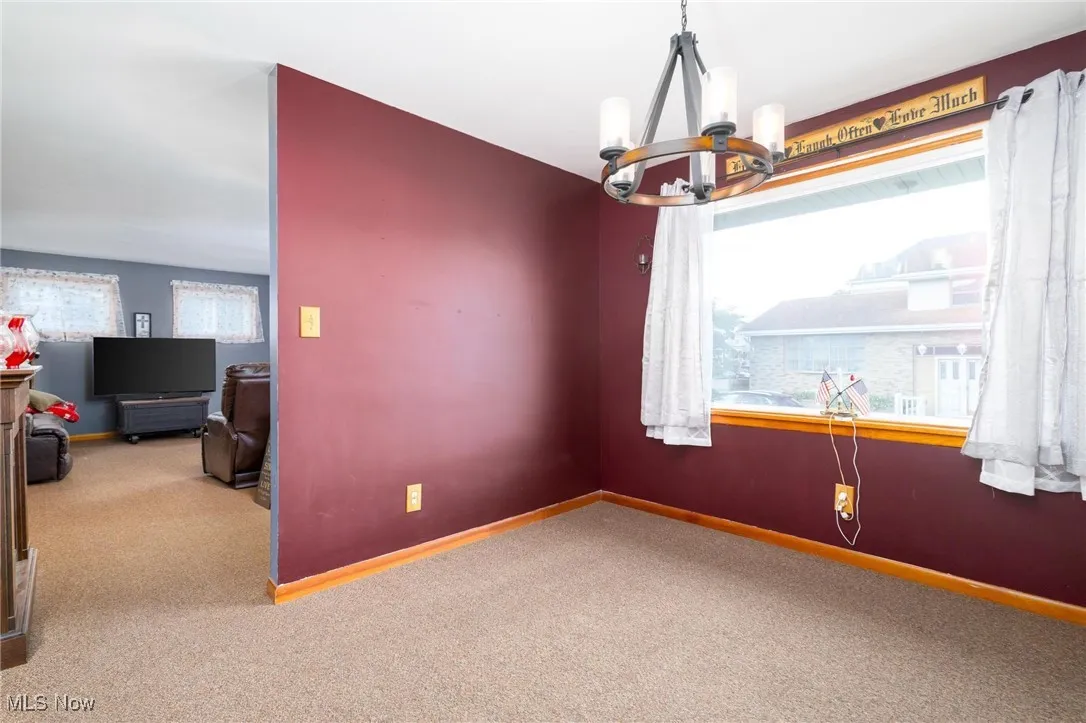 Unfurnished room featuring healthy amount of natural light, a chandelier, and carpet