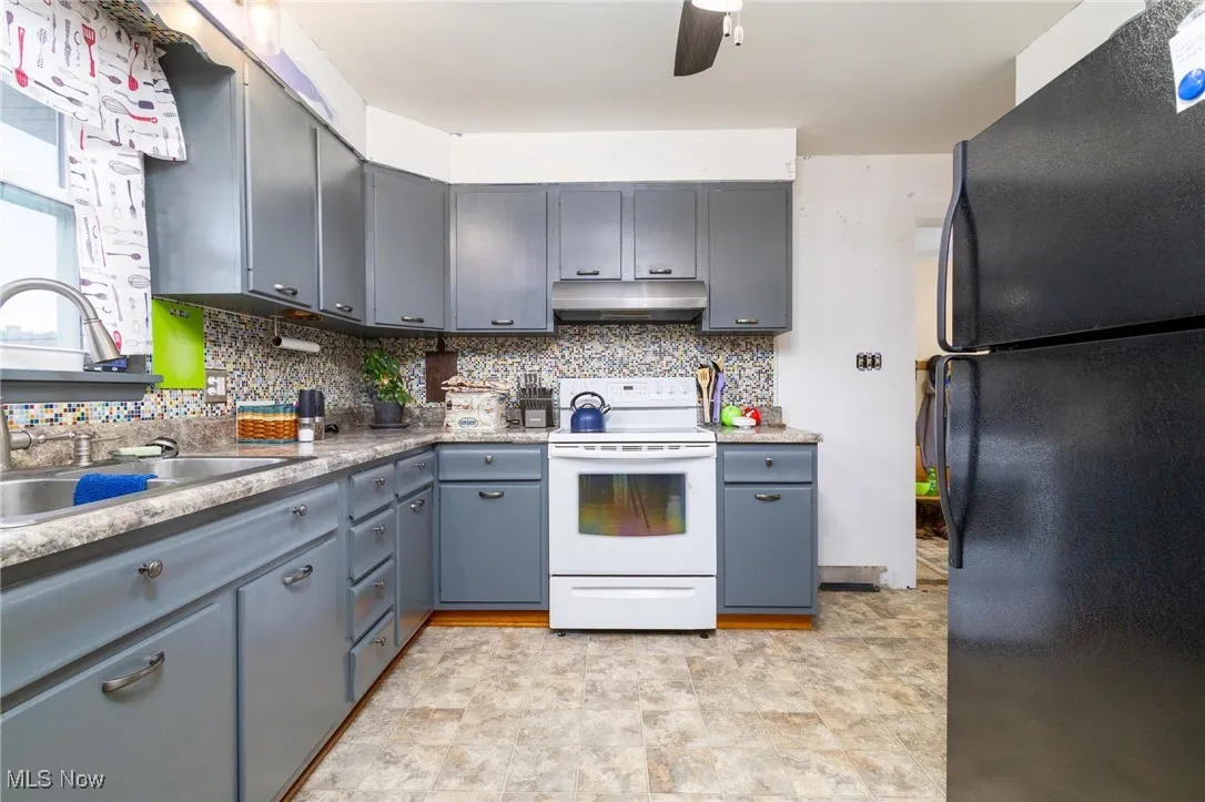 Kitchen with freestanding refrigerator, decorative backsplash, electric range, gray cabinets, and light countertops