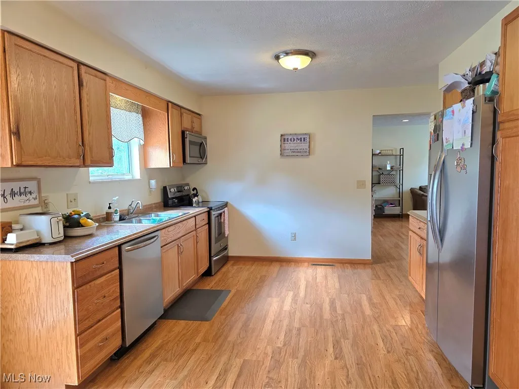 Kitchen featuring appliances with stainless steel finishes, light wood-style floors, light countertops, brown cabinets, and a textured ceiling