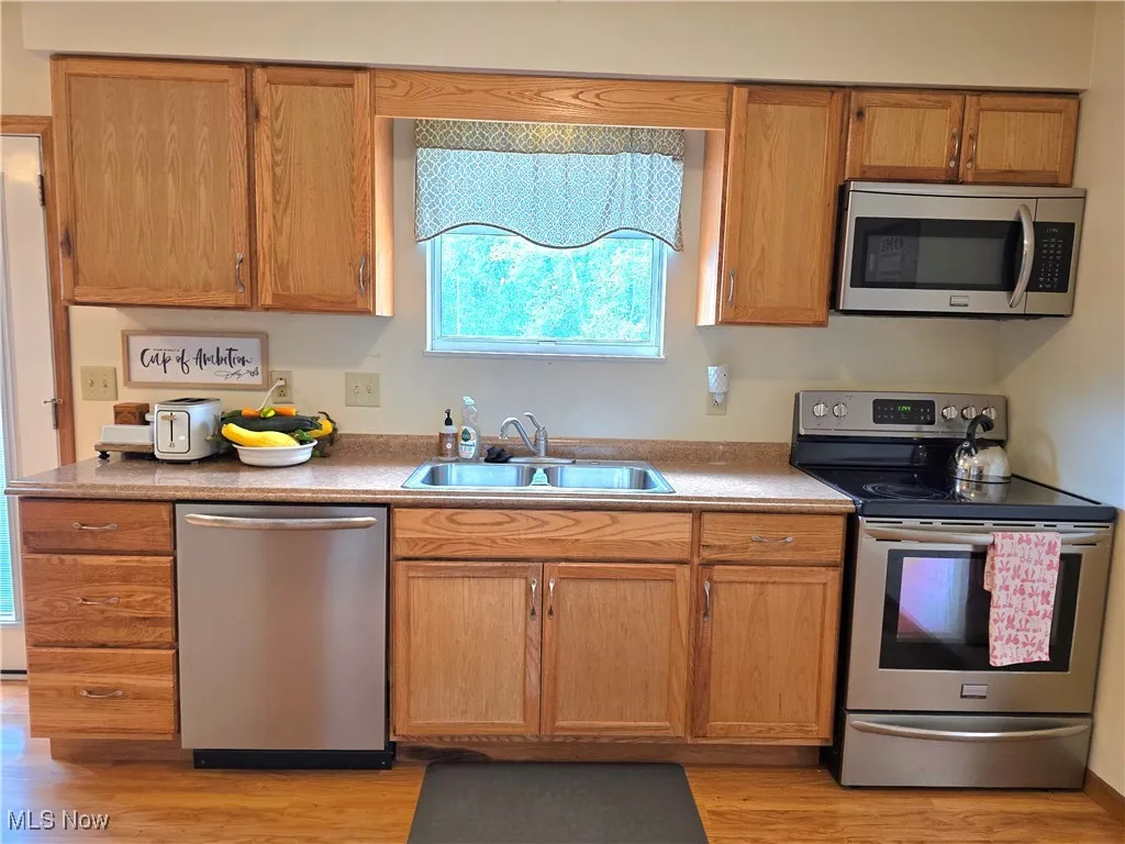Kitchen featuring plenty of natural light, appliances with stainless steel finishes, light wood-style flooring, and brown cabinetry