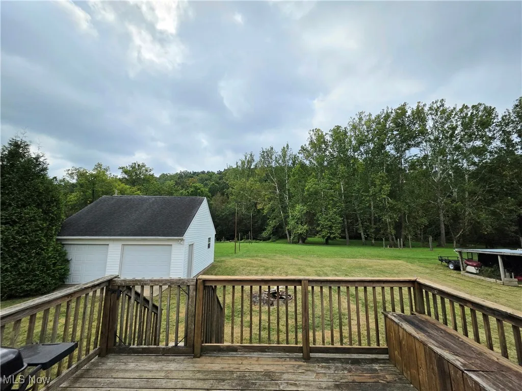 Deck with an outbuilding, a detached garage, a yard, and a view of trees