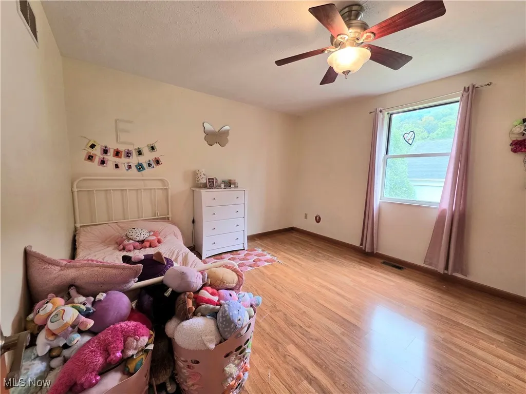 Bedroom with light wood-style floors, ceiling fan, and a textured ceiling