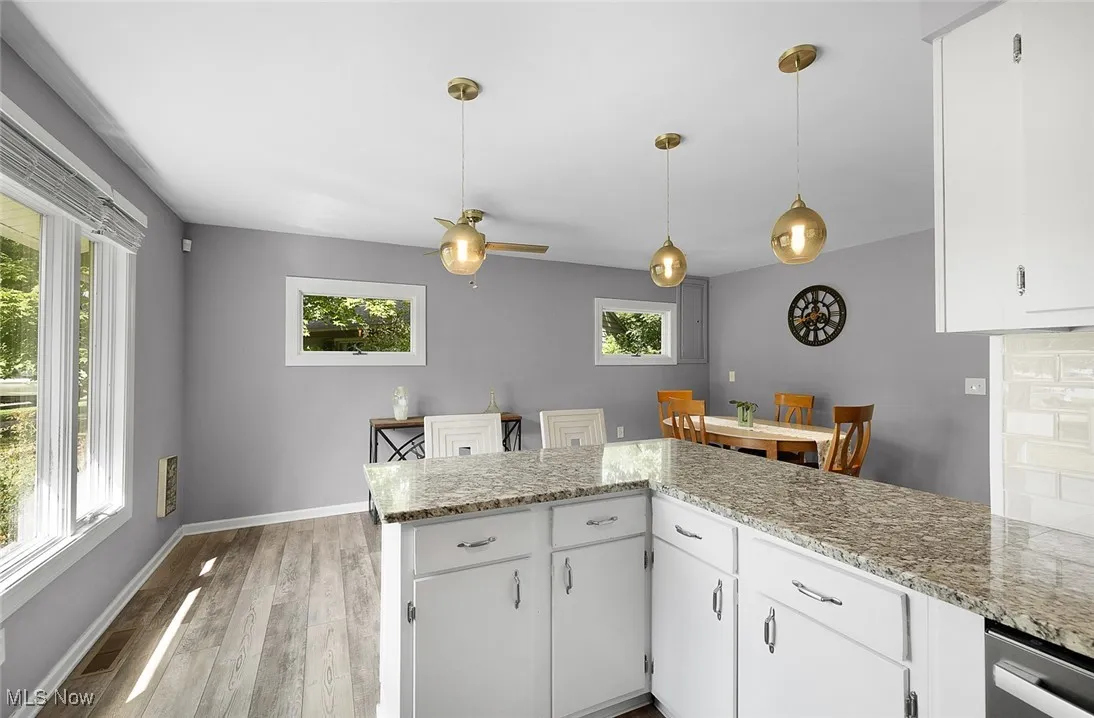 Kitchen with white cabinetry, light stone counters, light wood-style flooring, and hanging light fixtures