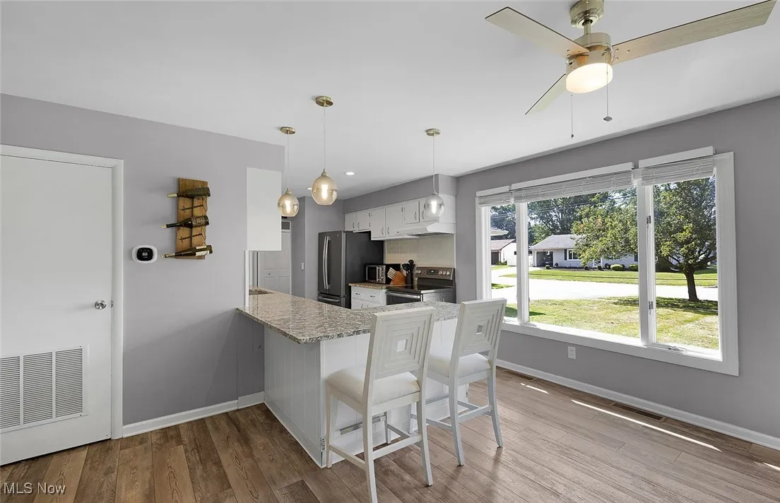 Kitchen featuring a breakfast bar area, light stone countertops, stainless steel appliances, decorative light fixtures, and white cabinets