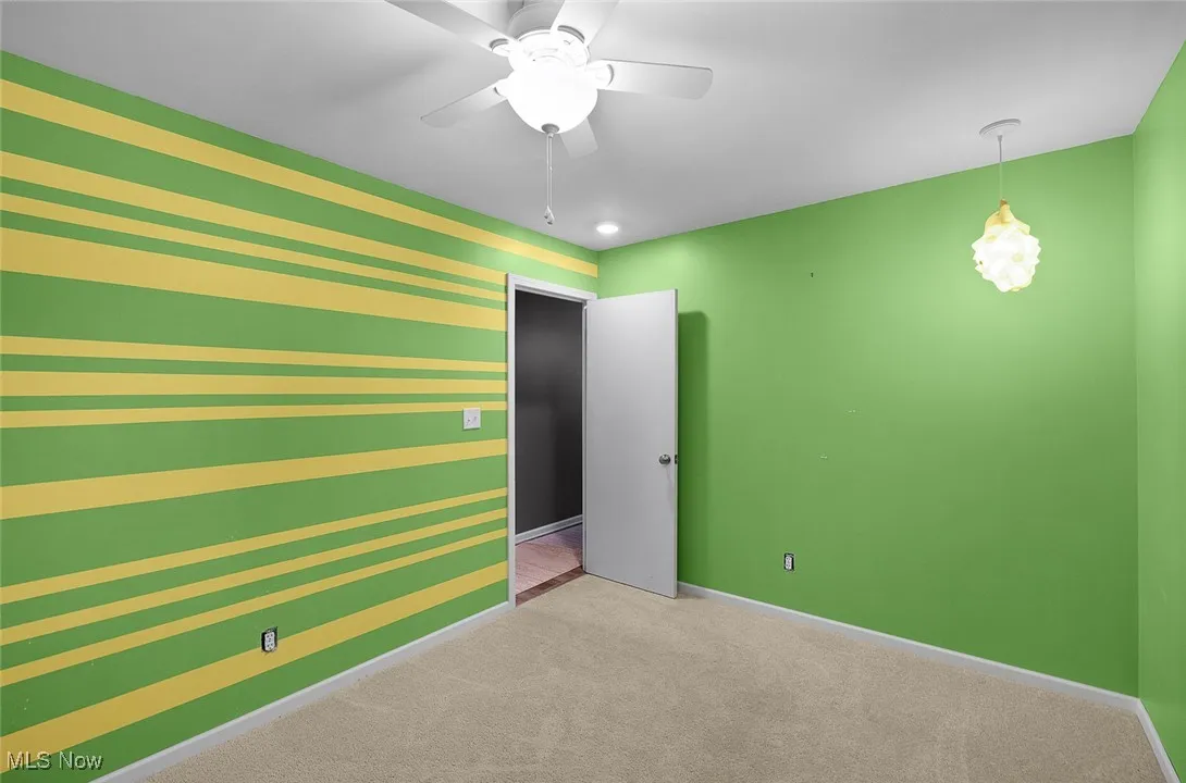 Unfurnished bedroom with carpet, an accent wall, and a ceiling fan