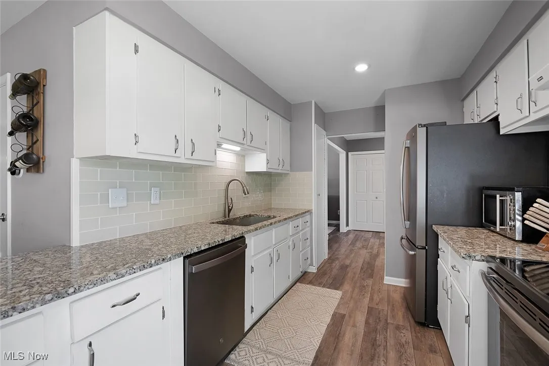 Kitchen featuring light stone countertops, backsplash, stainless steel appliances, dark wood-style flooring, and white cabinetry