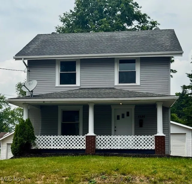 View of front of home with covered porch, an outbuilding, a front lawn, and roof with shingles