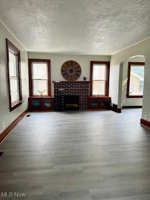 Unfurnished living room featuring a textured ceiling, wood finished floors, healthy amount of natural light, and a fireplace