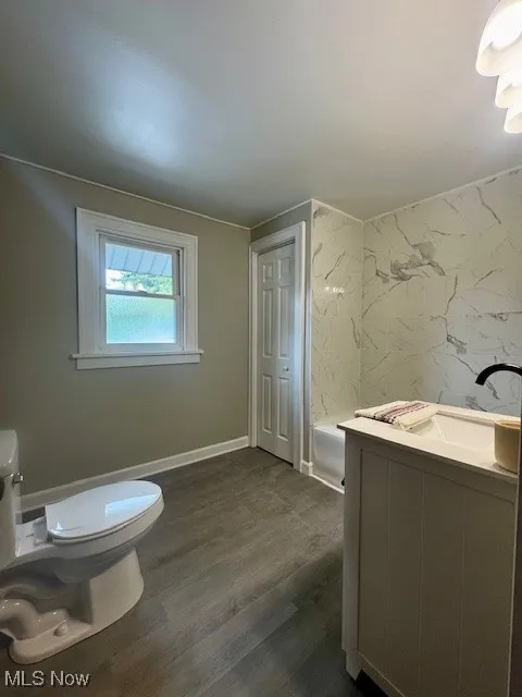 Full bathroom featuring toilet, a tub, vanity, and wood finished floors