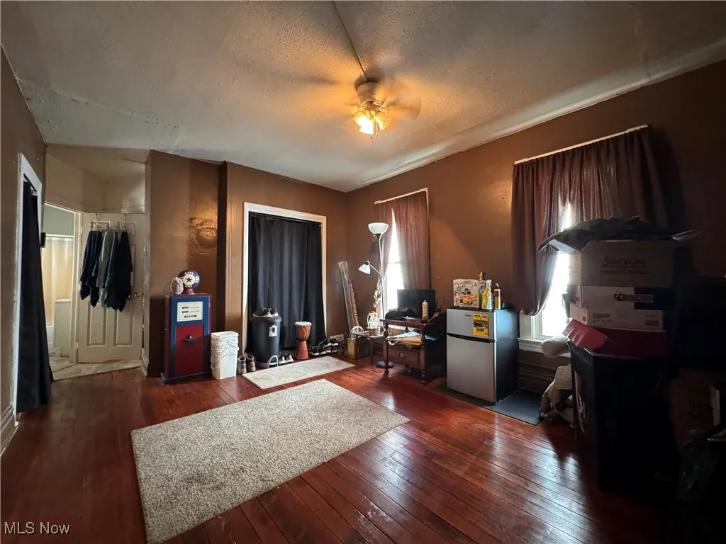 Bedroom with freestanding refrigerator, wood-type flooring, a textured ceiling, and a ceiling fan