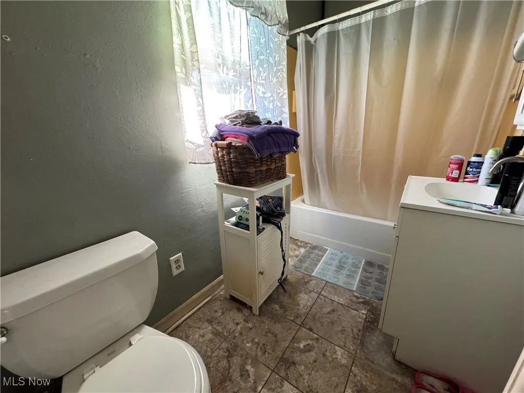 Full bathroom featuring shower / tub combo, a textured wall, vanity, and dark tile patterned flooring