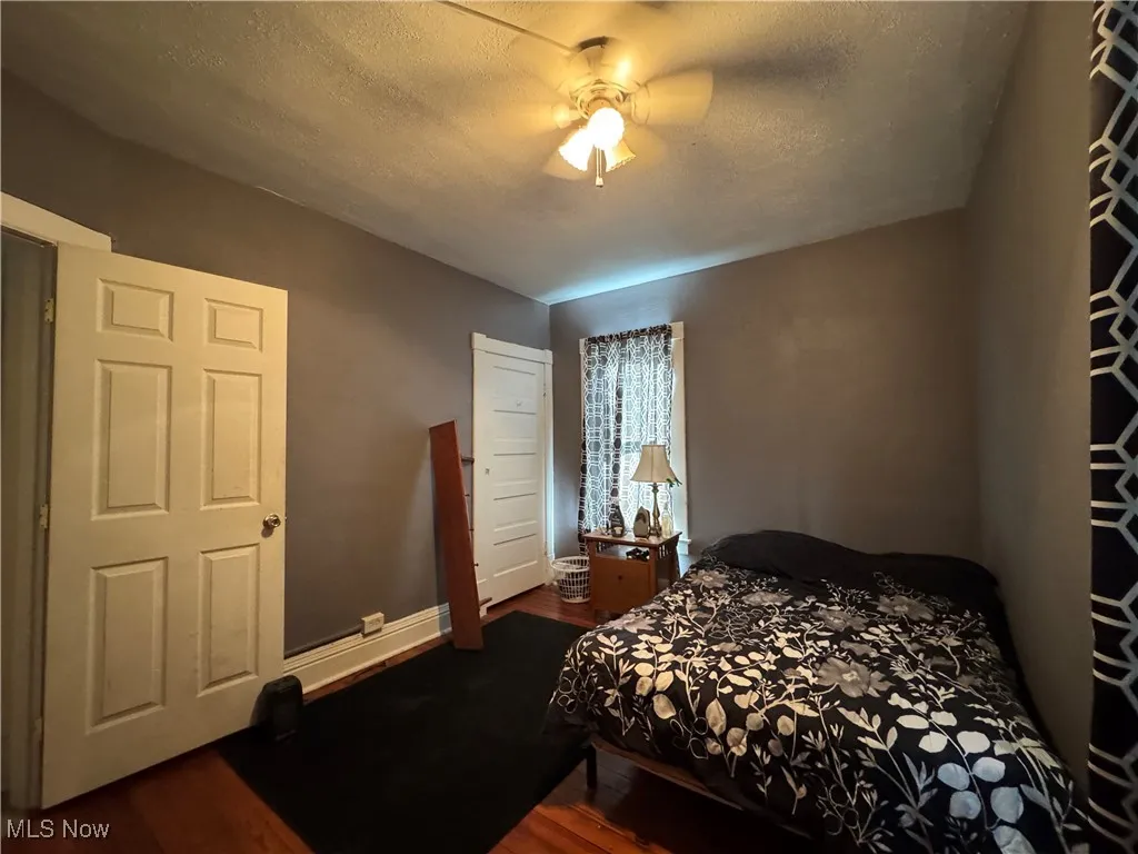 Bedroom with a textured ceiling, dark wood-style floors, and a ceiling fan