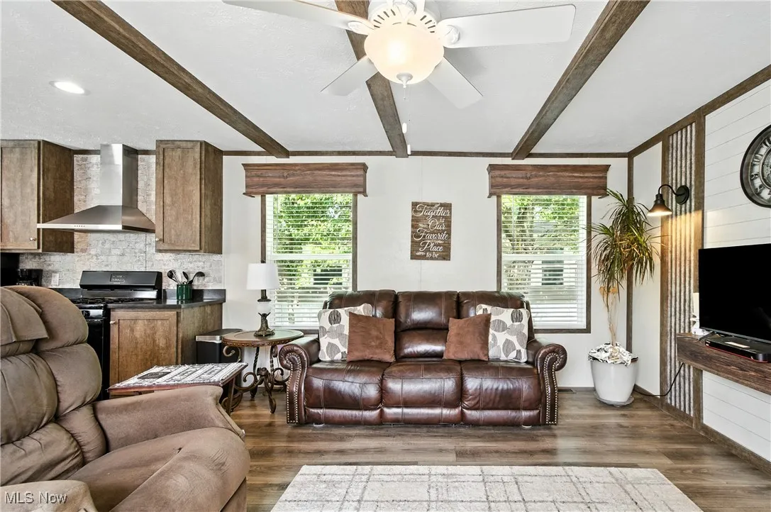 Living area featuring beam ceiling, plenty of natural light, dark wood finished floors, and ceiling fan