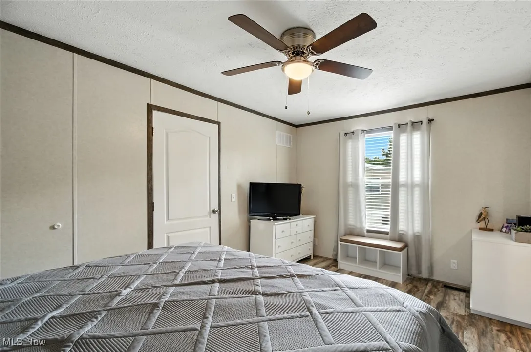 Bedroom with ornamental molding, a textured ceiling, wood finished floors, and a ceiling fan