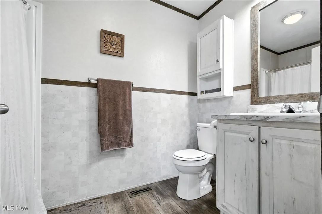 Bathroom with tile walls, crown molding, vanity, a wainscoted wall, and dark wood-style flooring