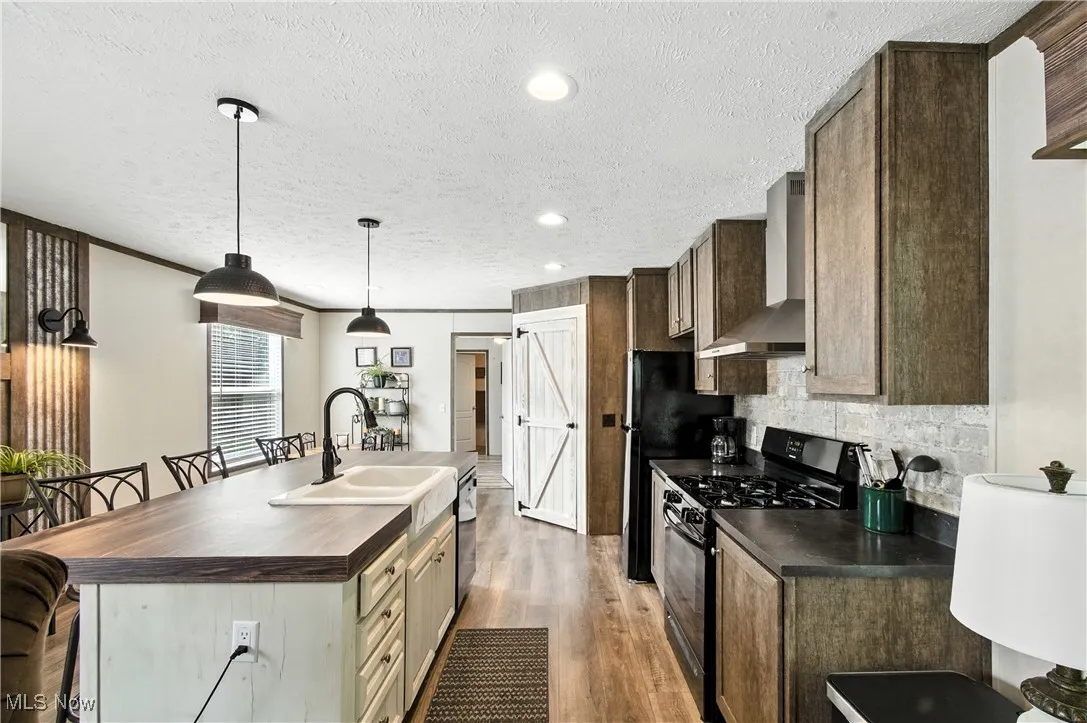 Kitchen featuring a breakfast bar area, black appliances, wooden counters, a center island with sink, and dark wood finished floors