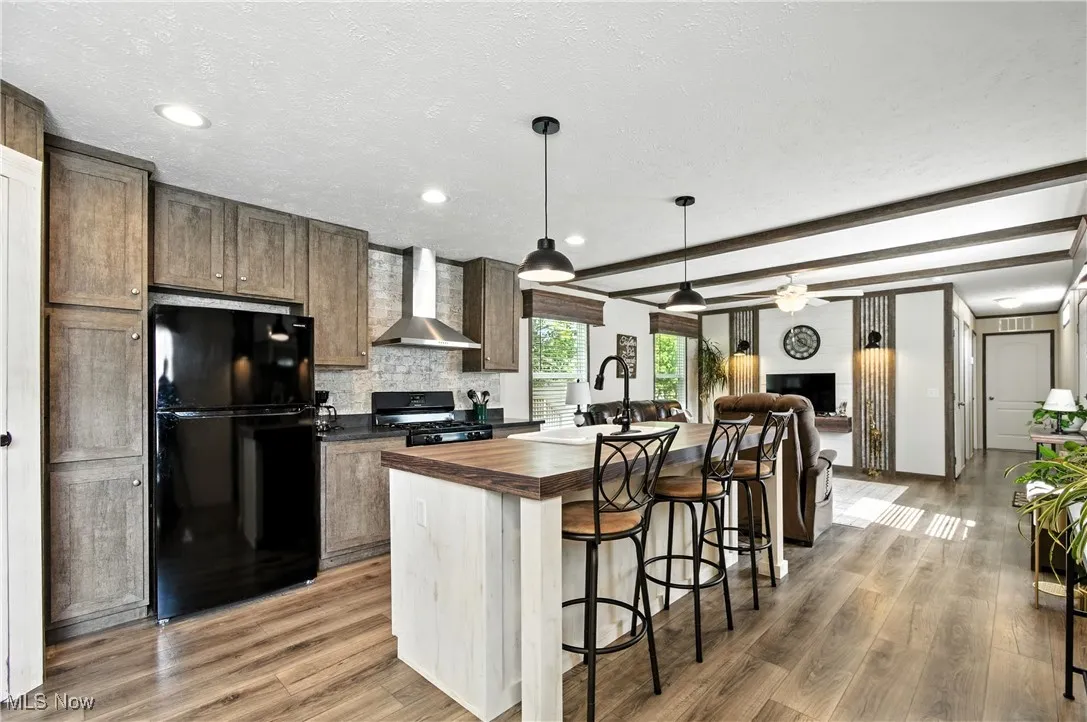 Kitchen with a kitchen breakfast bar, an island with sink, black appliances, butcher block countertops, and open floor plan