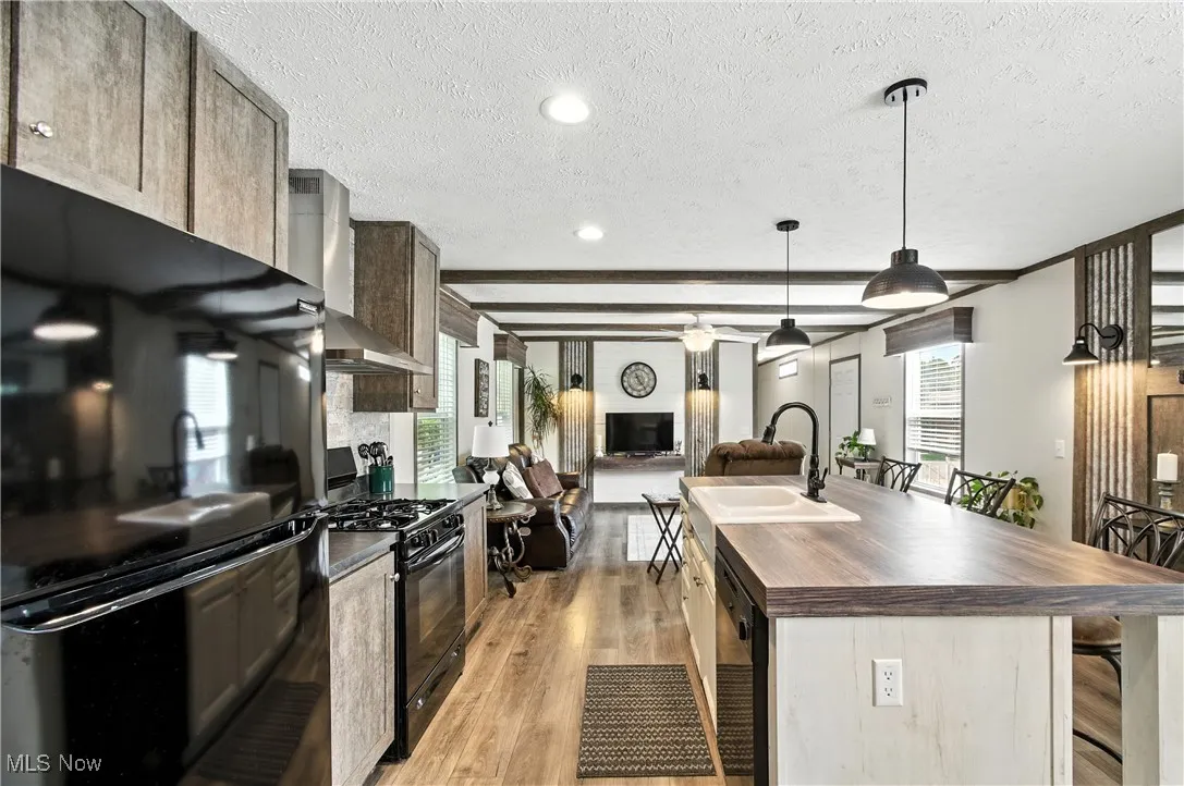 Kitchen featuring wooden counters, black appliances, a breakfast bar area, light wood finished floors, and a kitchen island with sink