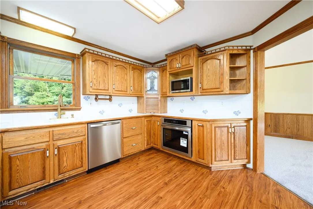 Kitchen featuring light countertops, crown molding, appliances with stainless steel finishes, brown cabinetry, and decorative backsplash