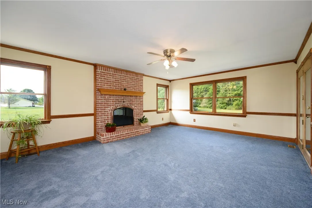 Unfurnished living room with a fireplace, carpet flooring, ornamental molding, and ceiling fan
