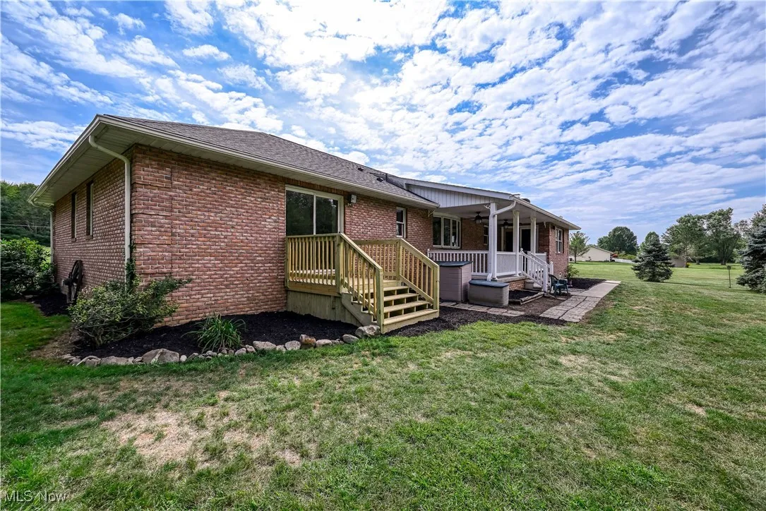 Rear view of property featuring brick siding, a deck, a lawn, and roof with shingles