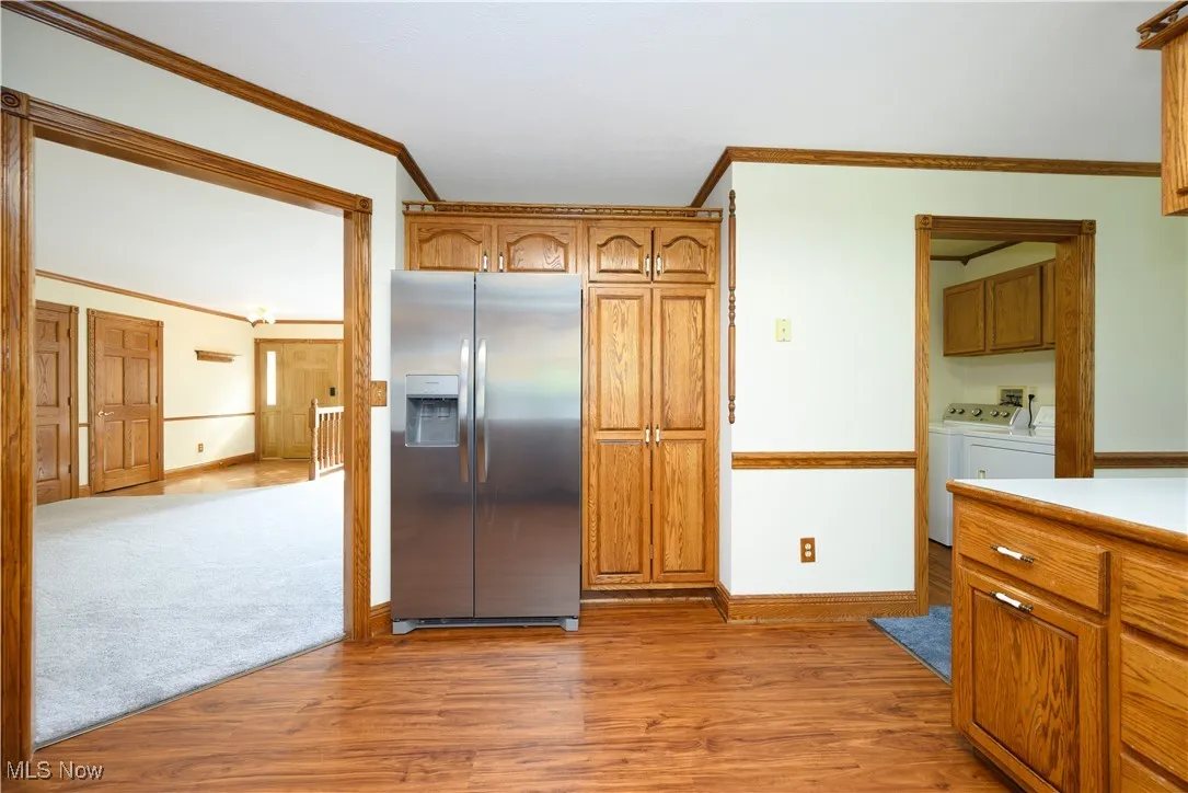 Kitchen featuring brown cabinets, ornamental molding, stainless steel refrigerator with ice dispenser, light countertops, and light wood-type flooring